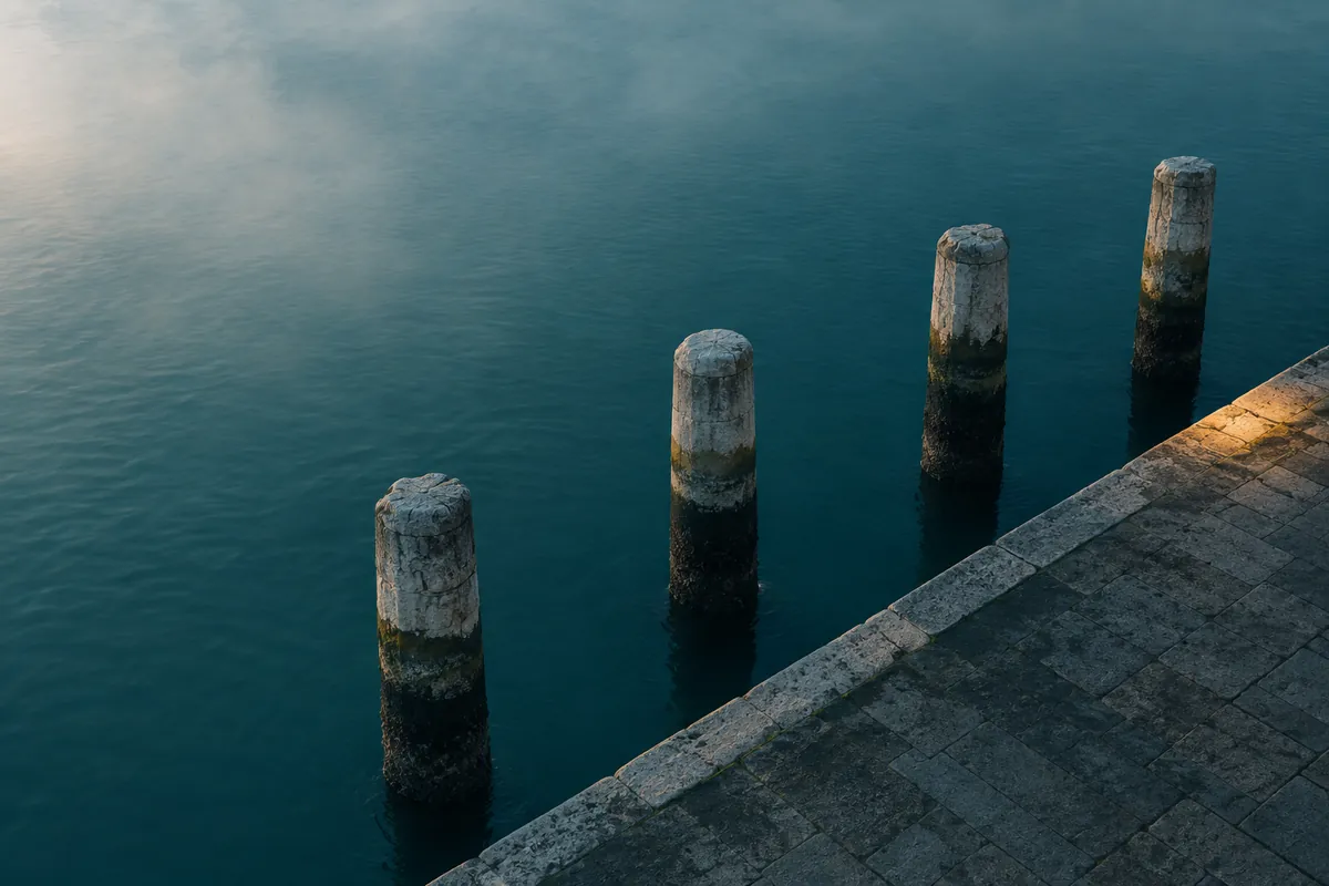 Four weathered stone pilings along a quay seen from above at dawn, each with a band of tide wear at a different height.